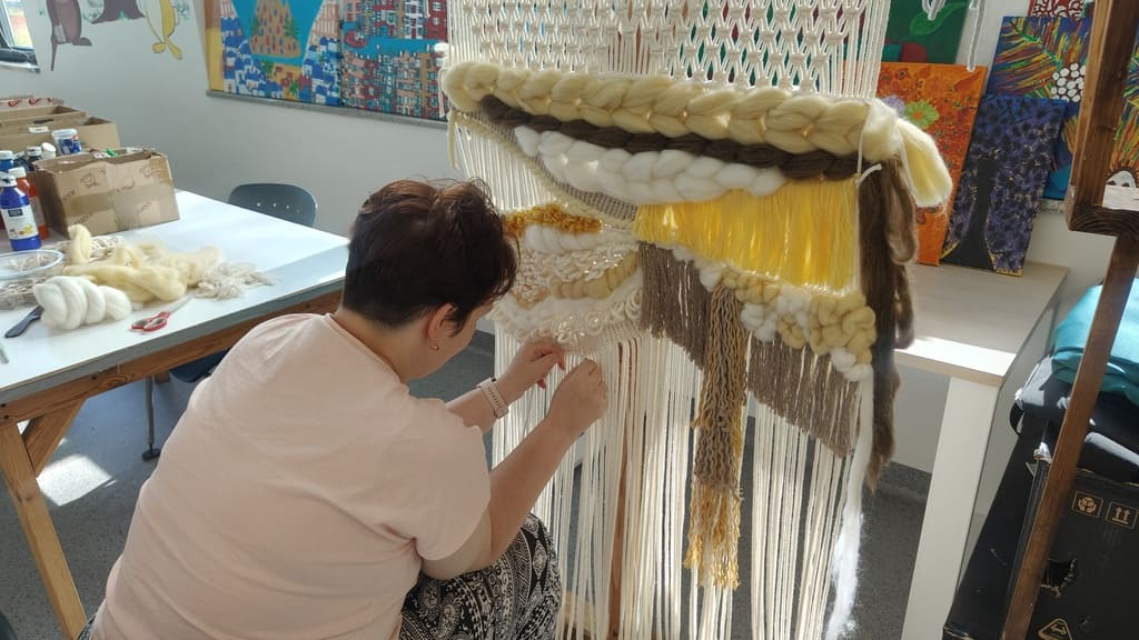 Tkactwo – uczestniczka tworzy makramę na krośnie